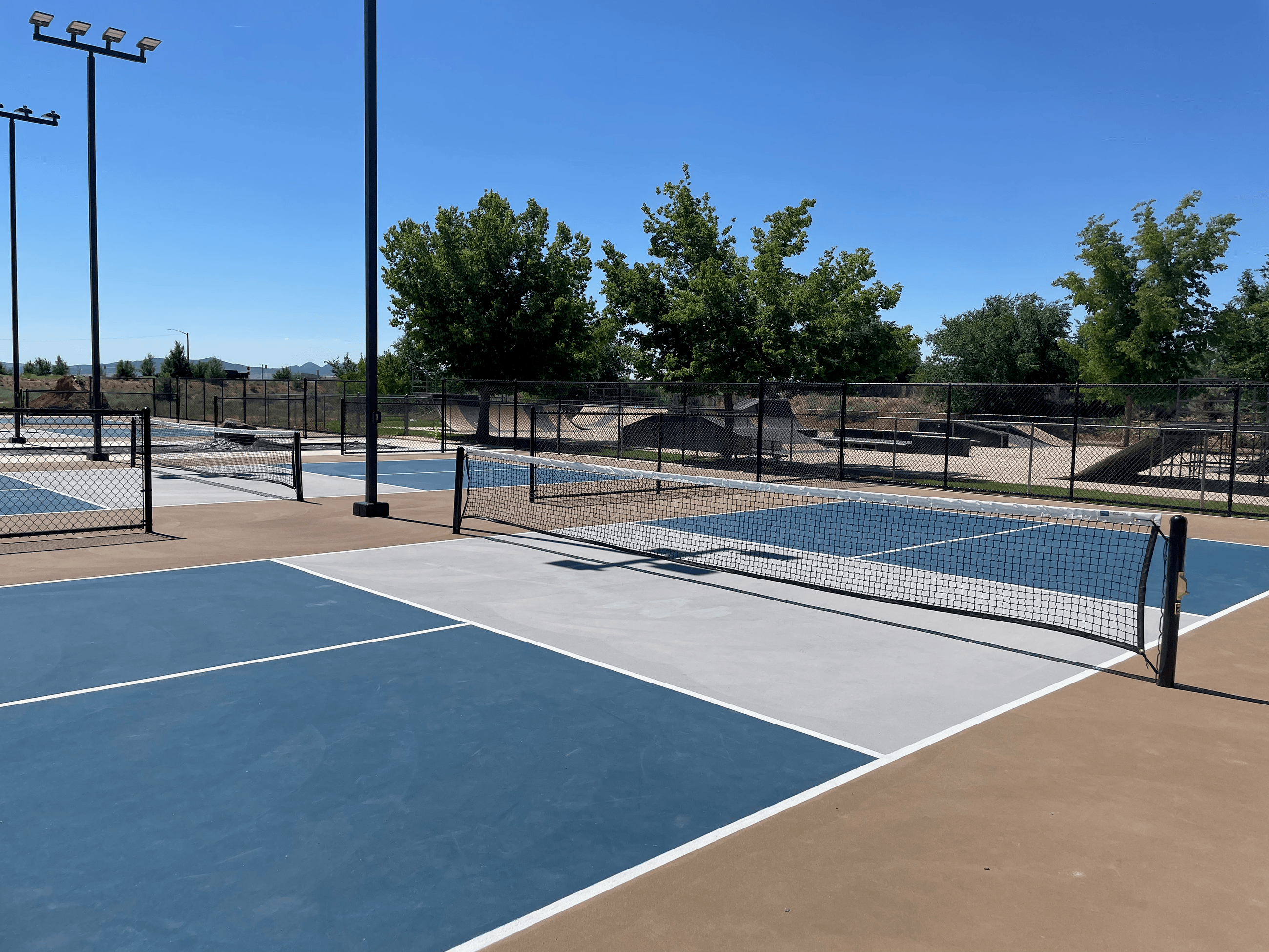 Image of blue pickleball courts with blue sky and green trees